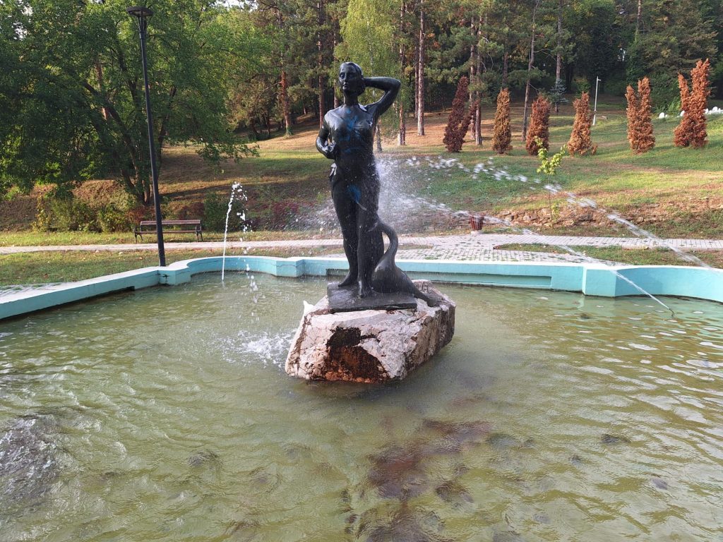 Fontana na Slanoj Banji u Tuzli sa skulpturom žene, okružena zelenilom i parkovskim sadržajima.